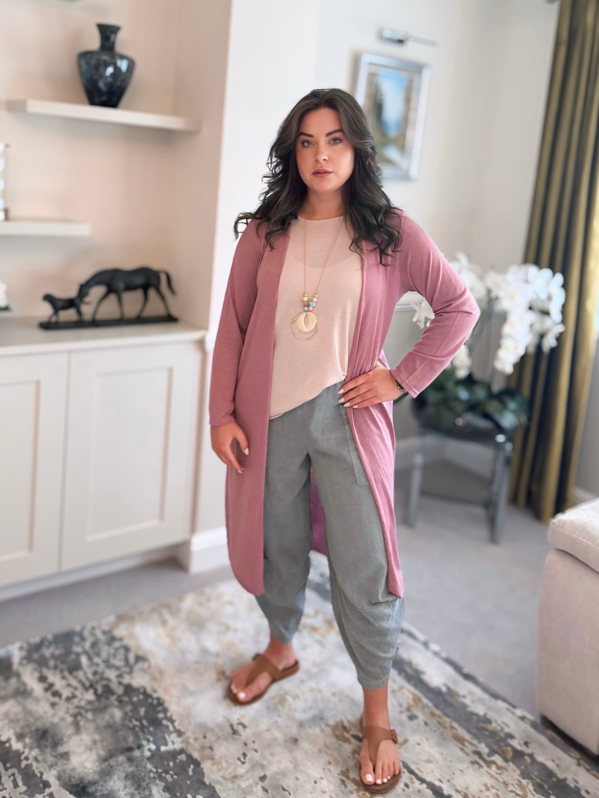 Woman in a pink cardigan and gray pants standing in a living room.