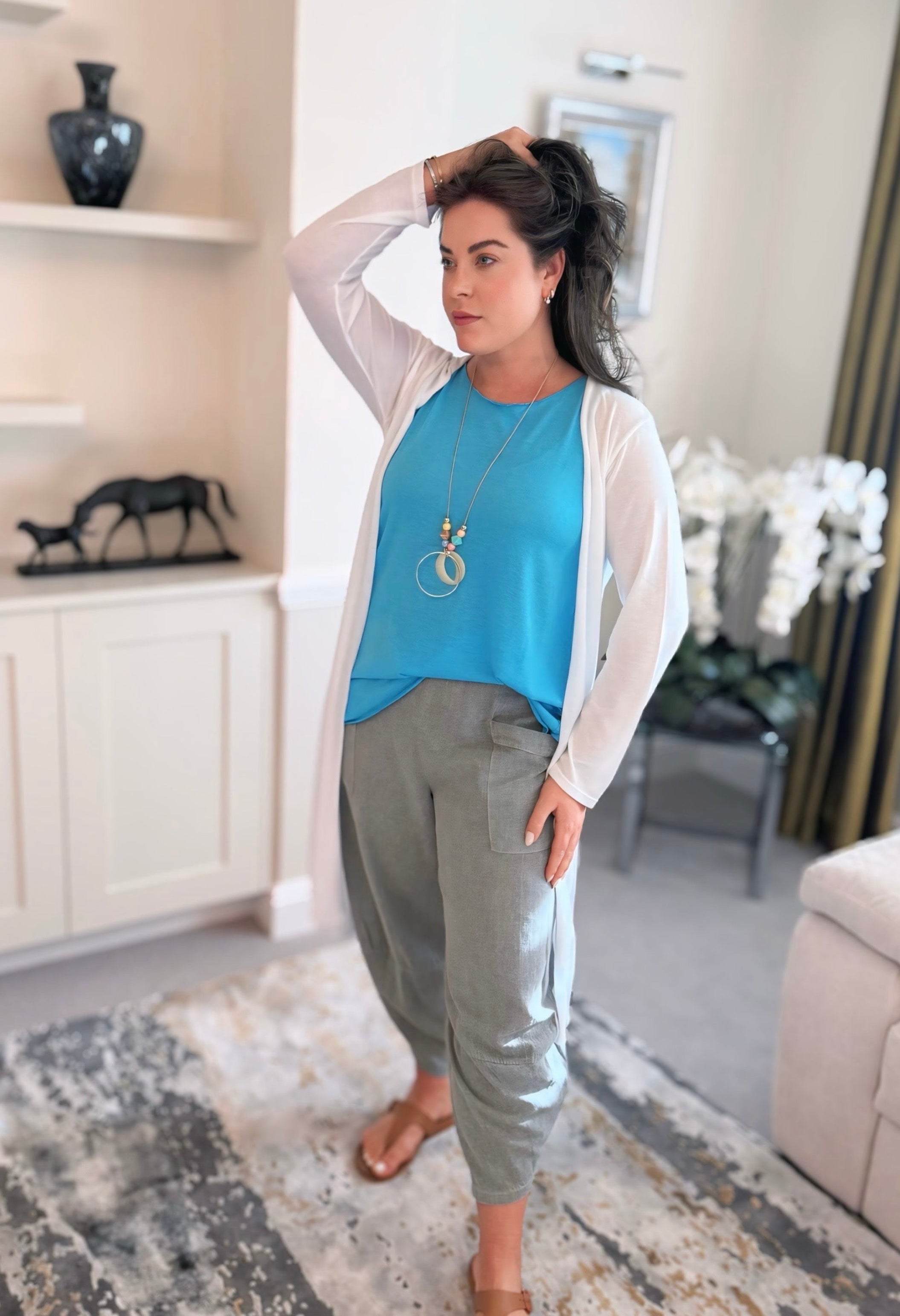 Woman standing in a living room wearing a blue vest and cotton harem pants 