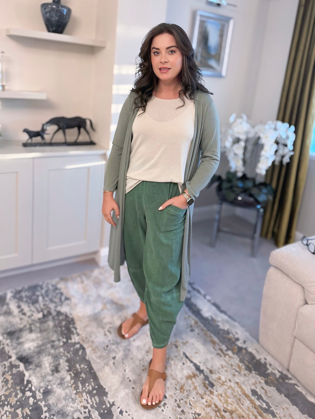 Woman in a green cardigan and cotton harem pants standing in a living room.