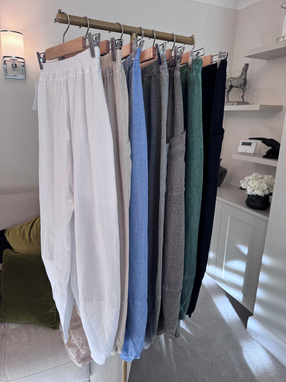 Row of cotton harem pants hanging on a rack in a room with a white cabinet and decorative items.