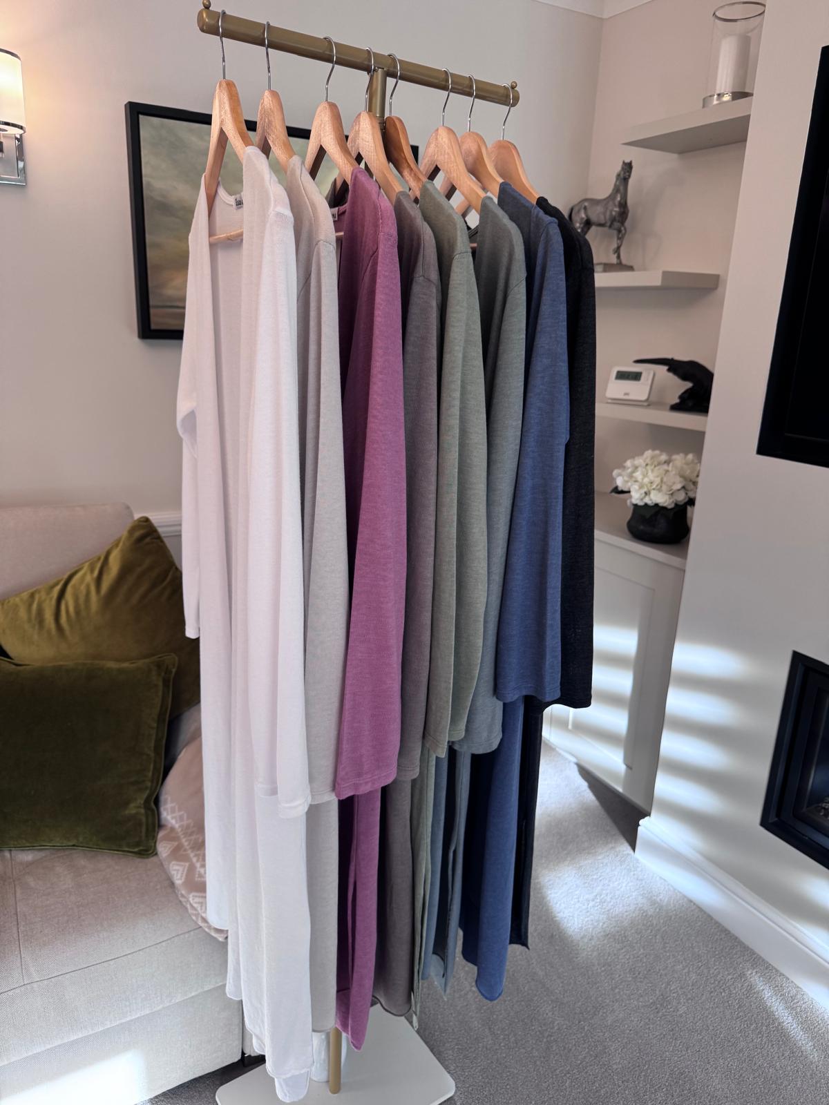 Row of long line cardigans  on hangers in a room with a couch and decor.